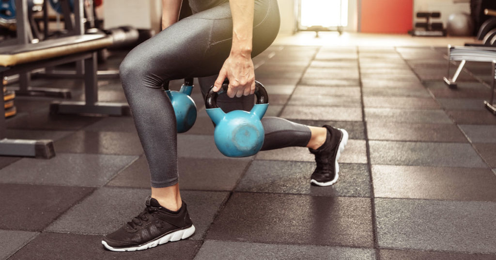 Imagen mujer haciendo zancada con pesas rusas 
